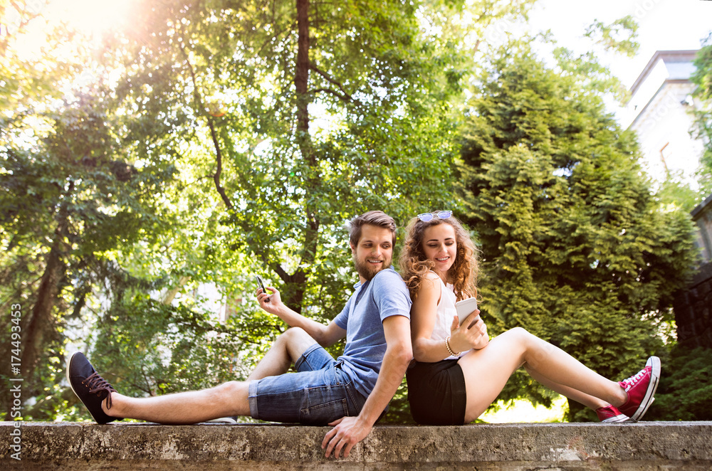 Young couple with smartphones in town sitting on concrete wall. Young couple with smartphones in town sitting on concrete wall.