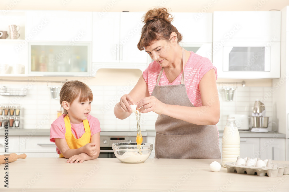 Cute little girl and her grandmother making dough on kitchen