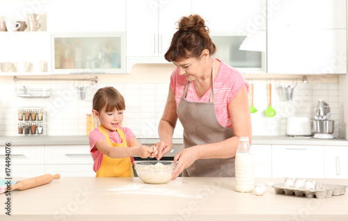 Cute little girl and her grandmother making dough on kitchen