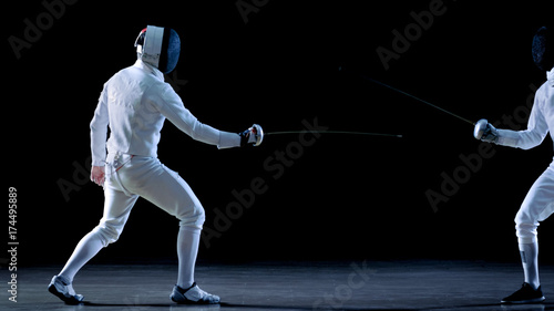 Two Professional Fencers Show Masterful Swordsmanship in their Foil Fight. They Dodge, Leap and Thrust and Lunge. Shot Isolated on Black Background.