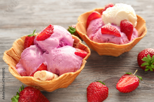 Delicious strawberry ice-cream in waffle bowls on wooden background