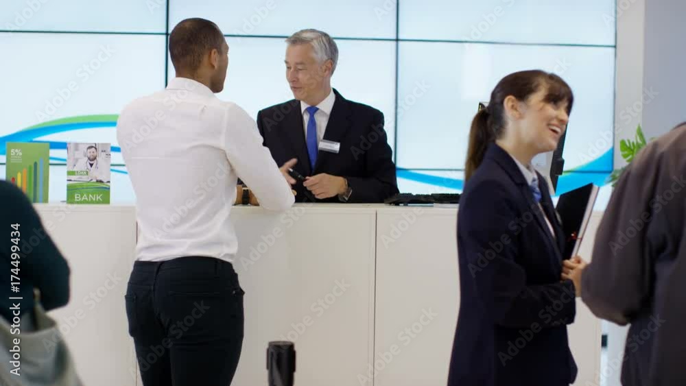 Friendly bank worker at service desk assisting customers with enquiries Friendly bank worker at service desk assisting customers with enquiries