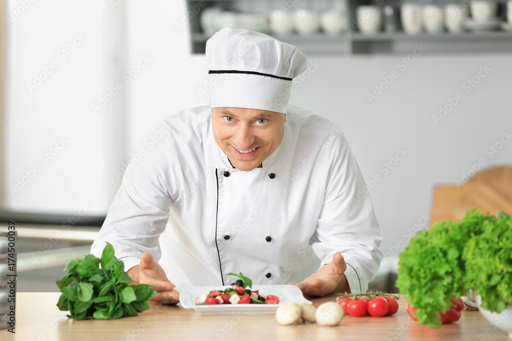 Male chef in uniform with salad on kitchen table Male chef in uniform with salad on kitchen table