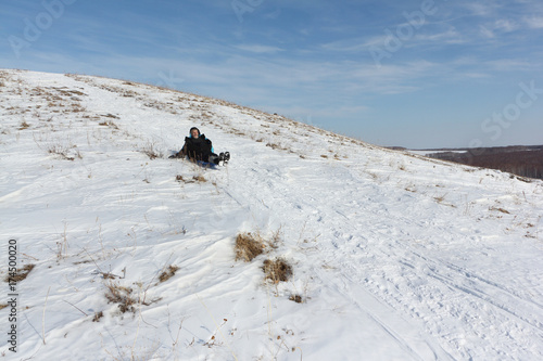 Man in a black jacket riding a mountain on a plastic sled in winter, Russia, Bugotak Hills © Nataliia Makarova