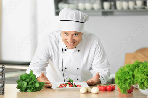 Male chef in uniform with salad on kitchen table