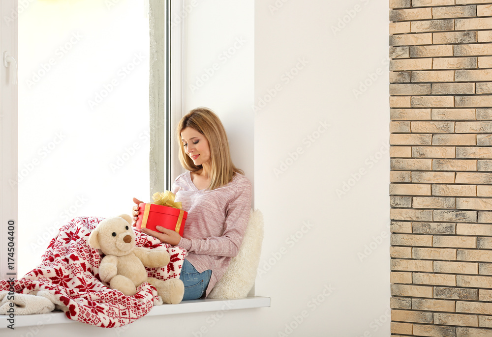 Young beautiful woman with gift box sitting on window sill. Christmas holiday concept Young beautiful woman with gift box sitting on window sill. Christmas holiday concept