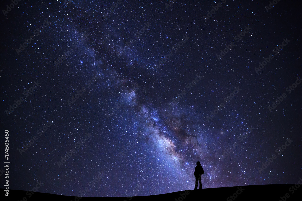 Naklejka premium Landscape with milky way galaxy, Starry night sky with stars and silhouette of a standing man on high mountain.