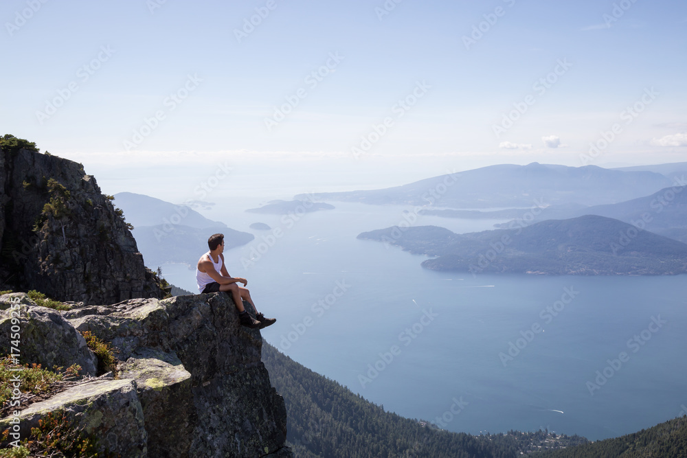 Fit and Adventurous Latin American man is hiking on top of a mountain ridge with a beautiful ocean view in the background. Taken at Lions Peaks, North of Vancouver, British Columbia, Canada.
