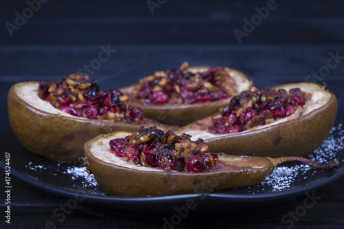 Homemade baked pears with honey, red cranberries and walnuts in black plate, close up