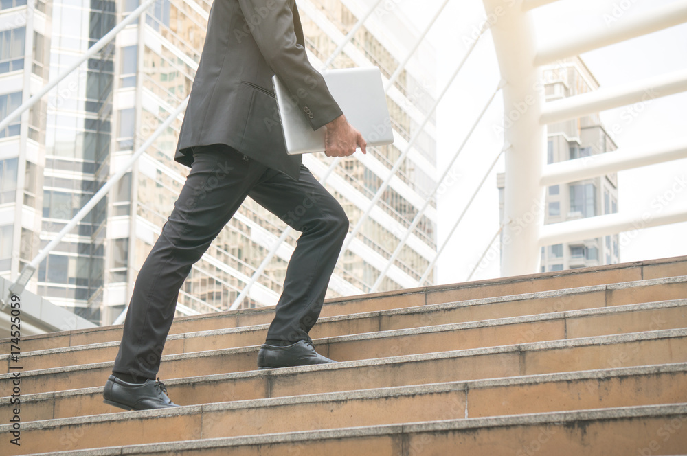 Businessman holding laptop step up on stair to future with building background in city outdoor Businessman holding laptop step up on stair to future with building background in city outdoor