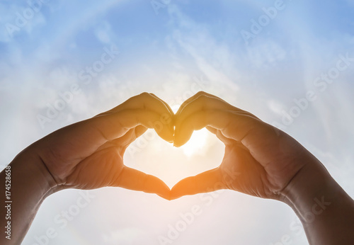 Silhouette two hands making form heart shape with sun halo background 