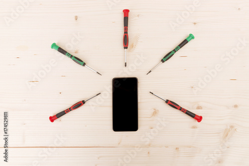 Mobile phone repair. Phone with screwdrivers around on wooden background 