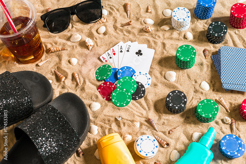 Gambling on vacation concept - white sand with seashells , colored poker chips and cards. Top view