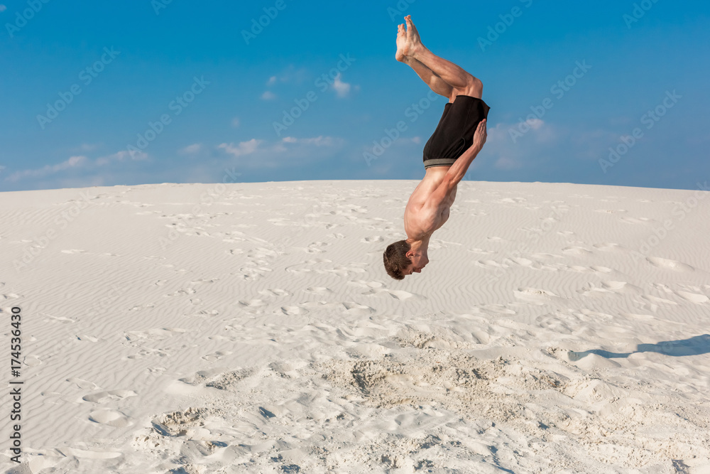 Portrait of young parkour man doing flip or somersault on the sand. Portrait of young parkour man doing flip or somersault on the sand.