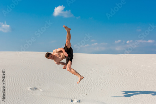 Foto Portrait of young parkour man doing flip or somersault on the sand