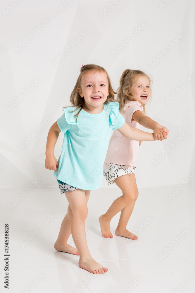 Two little funny and laughing girl in the identical clothes of different colors playing in white studio Two little funny and laughing girl in the identical clothes of different colors playing in white studio