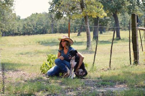Woman in western cowboy hat happy and holding her cute pet dog on the farm.