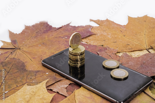 Smartphone on maple leaves background with some coins. photo