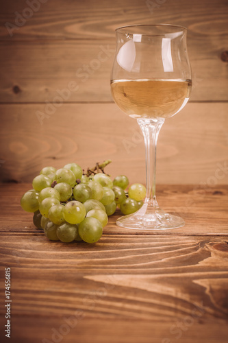 Glass of white wine and grapes on rustic wood table