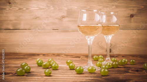 Two glasses of white wine and grapes on wooden table