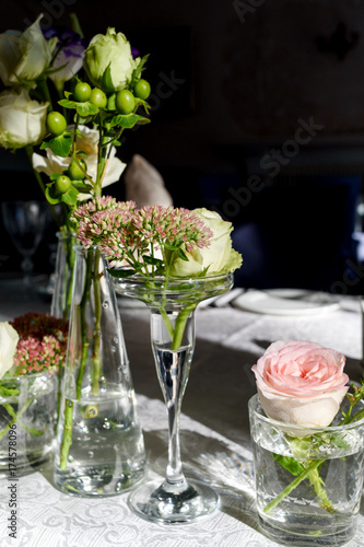 Beautiful fresh flowers on table in wedding day, free space. Wedding table decoration. Bouquet of pink roses and greenery in glass vases on dinner table in restaurant