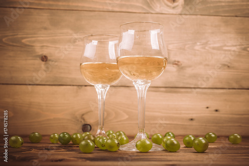 Two glasses of white wine and grapes on wooden table