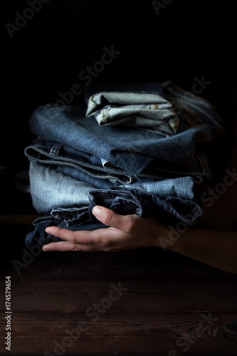 Cuadro en lienzo stack of blue jeans pants on the hands of a girl on a dark background with a co