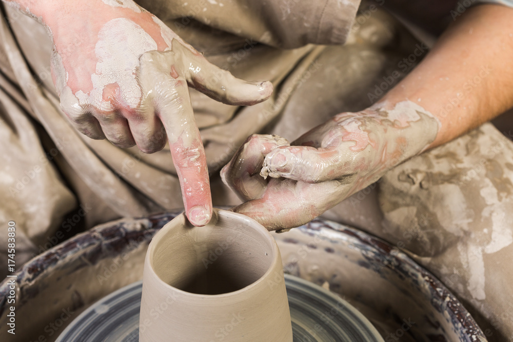 pottery, workshop, ceramics art concept - closeup on man's hands work with potter wheel and raw clay, male fingers sculpt some new utensils with water, top view