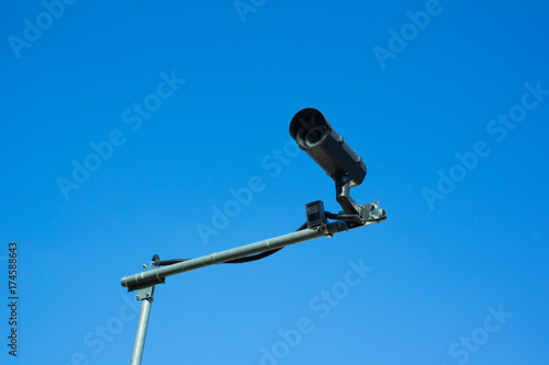 Security camera for surveillance, control, monitoring, spying and protection. Technological device is recording video. Clear blue sky in the background.