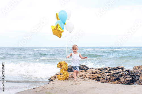 Boy running on a beach holding balloons