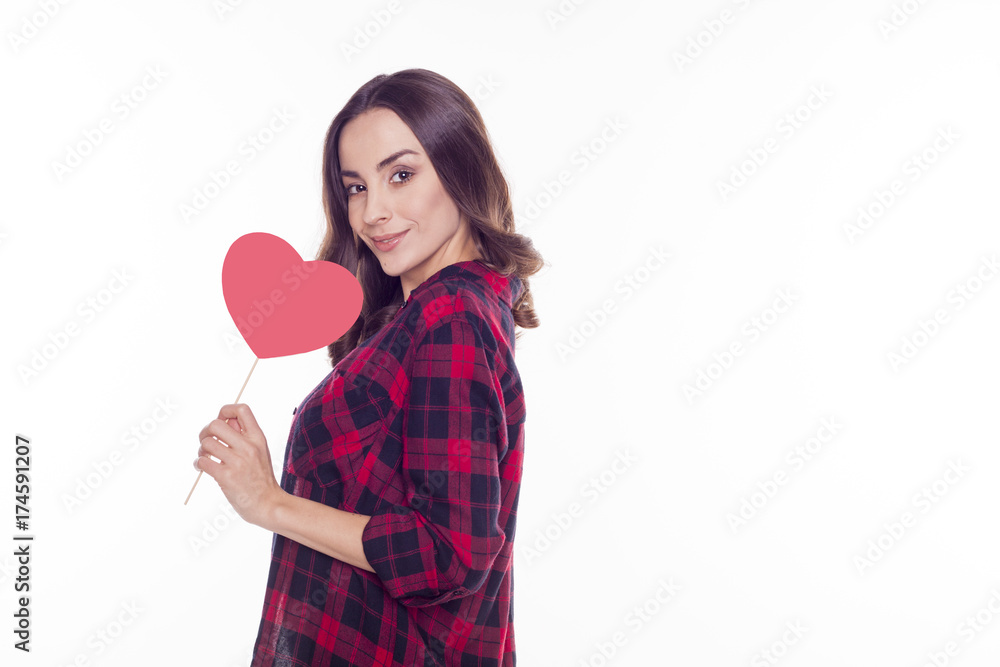 Young beautiful brunette girl smiles and holds in her hands a red paper heart isolated on white Young beautiful brunette girl smiles and holds in her hands a red paper heart isolated on white