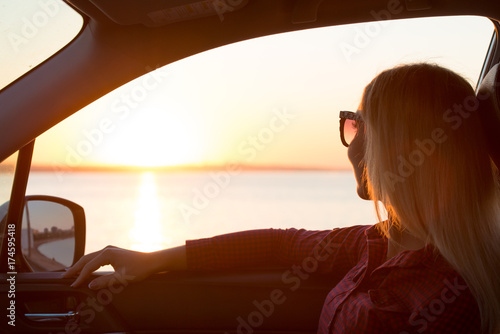 A young woman looks out the car window at the sunset on the sea.  © Denis