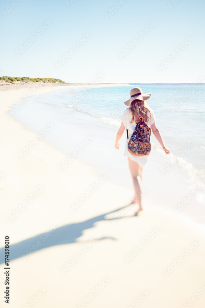 Teenage girl with hat and backpack walks along the white sand of Turquoise Bay after a day at the beach Teenage girl with hat and backpack walks along the white sand of Turquoise Bay after a day at the beach