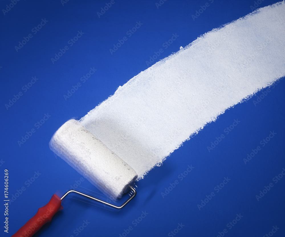 Obraz premium Paint roller applying white paint on blue wall background