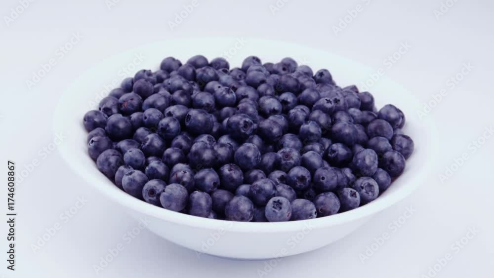 A white plate full of ripe fresh juicy blueberries is on a white table. Berry dessert. Preparation of fresh berries. A whole mountain of blueberries. Very berry blueberry cheesecake. Side view.