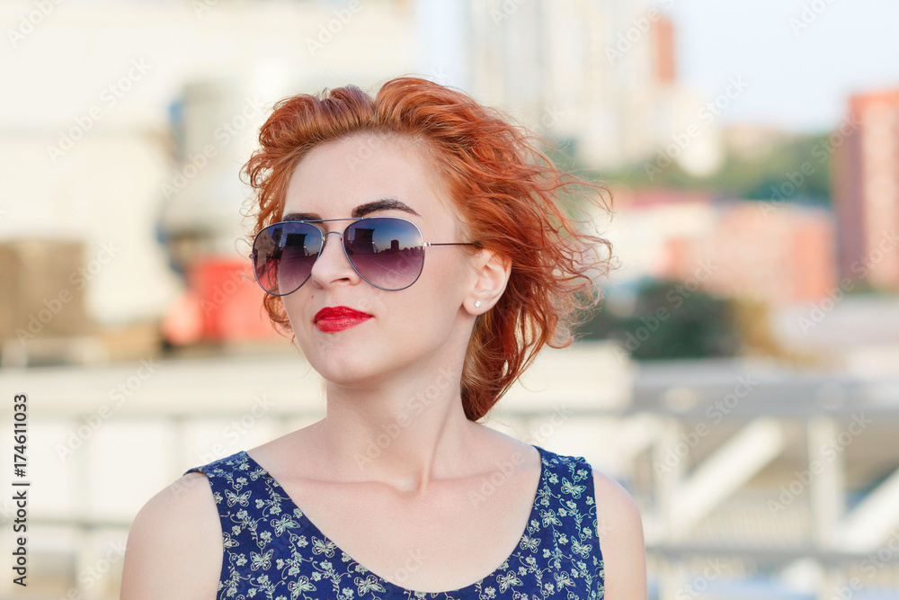 Young beautiful girl with beautiful appearance. Red-haired woman with a pretty face at sunset. A charming, smiling woman portrait  with a beautiful look, posing against the backdrop of the cityscape.