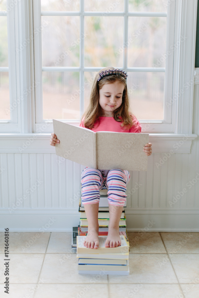 Cute young girl sitting on a stack of books reading Stock Photo | Adobe ...