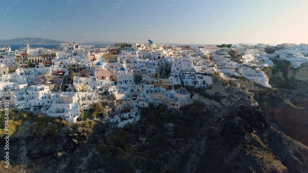 Aerial view of iconic white houses and blue dome churches on steep cliff, Santorini Island, Greece. Village of Oia. Morning light