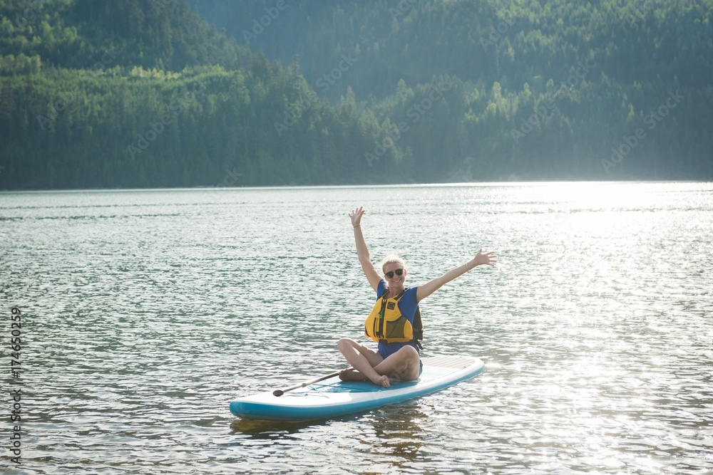 Excited young woman sitting on paddleboard in lake Excited young woman sitting on paddleboard in lake
