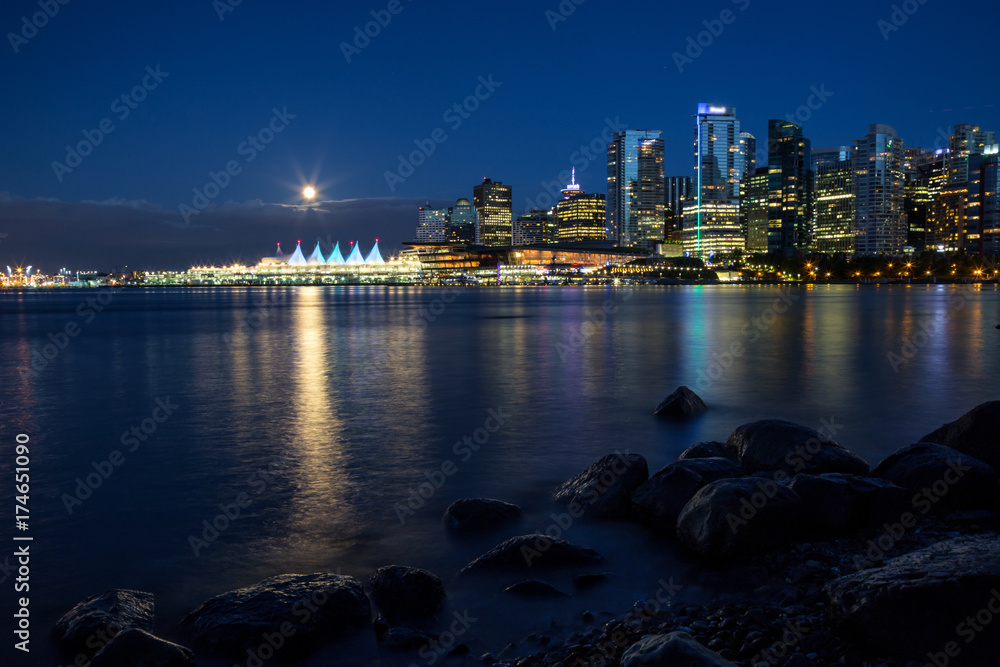 Beautiful view of Downtown Vancouver Skyline during the night with the full moon rising. Taken in Stanley Park around Coal Harbour, British Columbia, Canada.