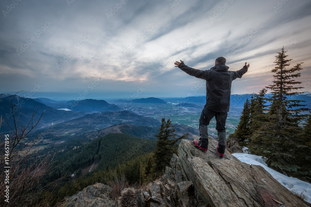 Man standing on top of a mountain with open arms and enjoying the beautiful scenery. Picture taken on top of Elk Mountain in Chilliwack, British Columbia, Canada, during a cloudy sunset. Man standing on top of a mountain with open arms and enjoying the beautiful scenery. Picture taken on top of Elk Mountain in Chilliwack, British Columbia, Canada, during a cloudy sunset.