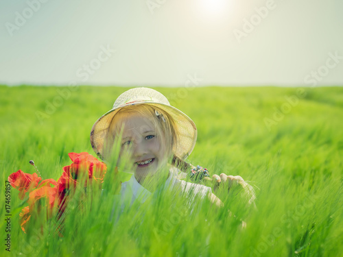Beautiful cheerful girl in a hat with a bouquet of tulips on a green field of rye.