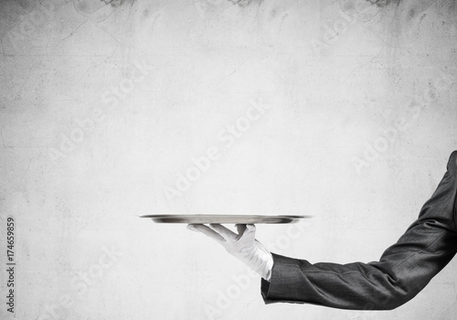 Hand of butler holding empty metal tray against concrete background