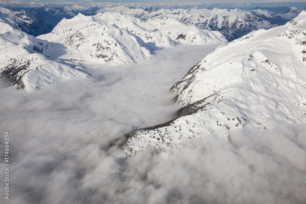Beautiful aerial landscape view of the snow covered mountain range with a low level cloud. Taken in the remote area early morning North West from Vancouver, British Columbia, Canada. Beautiful aerial landscape view of the snow covered mountain range with a low level cloud. Taken in the remote area early morning North West from Vancouver, British Columbia, Canada.