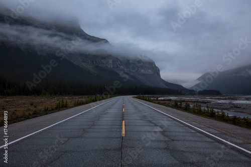 Gloomy and Moody picture of a Road with mountains in the background covered in clouds. Taken in Icefields Pkwy, Banff National Park, Alberta, Canada.