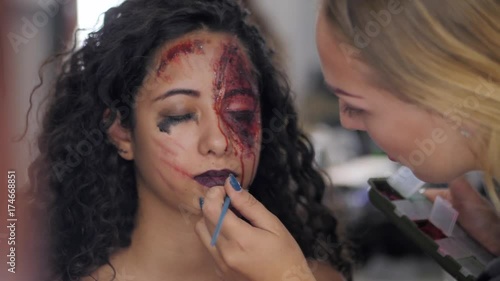 Make-up artist make the girl halloween make upin studio.Halloween face art.Woman applies on professional greasepaint on the face of spanish girl.War-paint with blood, scars and wounds.Slow motion. photo