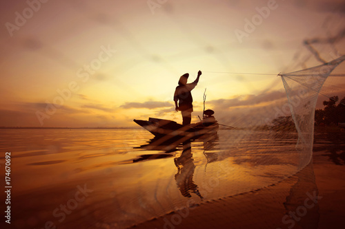 Fisherman is fishing on the boat by using net at sea while sunset. photo