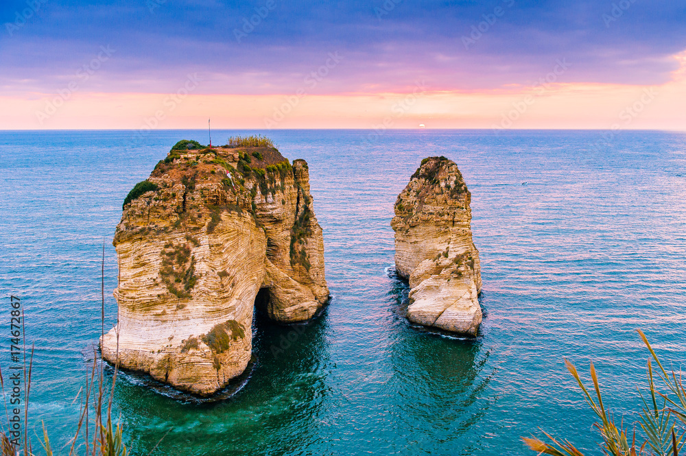 Obraz premium Piękny zachód słońca na Raouche, Pigeons 'Rock. W Bejrucie w Libanie Słońce i kamienie odbijają się w wodzie, gęste chmury na niebie.