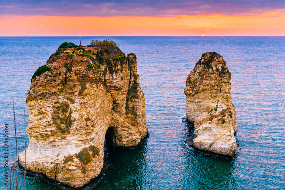 Obraz premium Piękny zachód słońca na Raouche, Pigeons 'Rock. W Bejrucie w Libanie Słońce i kamienie odbijają się w wodzie, gęste chmury na niebie.