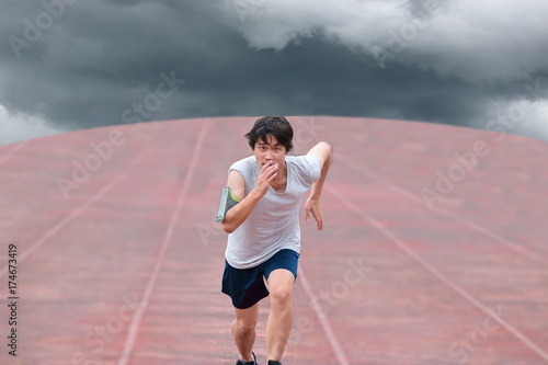 Young Asian runner running on track with weather storm on dark cloudy sky background. © tuaindeed